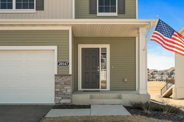 view of exterior entry featuring an attached garage, stone siding, and covered porch