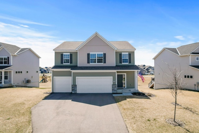 traditional-style house with a garage, stone siding, a front yard, and aphalt driveway