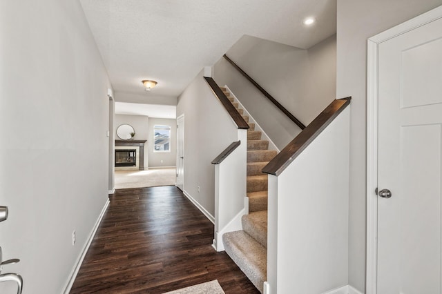 stairs featuring a glass covered fireplace, wood finished floors, baseboards, and recessed lighting
