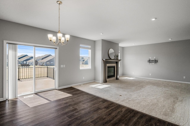 unfurnished living room with baseboards, a notable chandelier, a glass covered fireplace, and wood finished floors