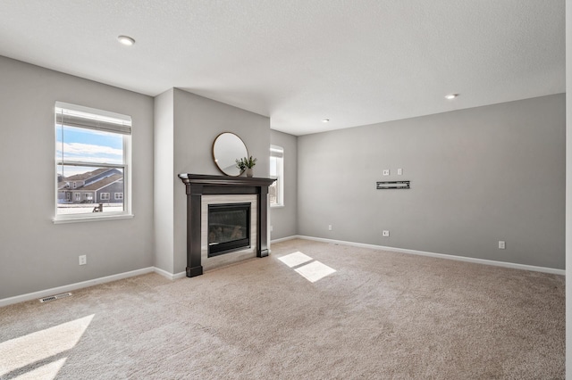 unfurnished living room featuring a glass covered fireplace, visible vents, carpet flooring, and baseboards