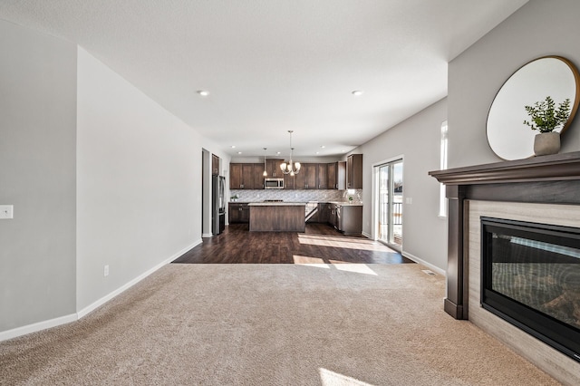 unfurnished living room featuring dark colored carpet, a glass covered fireplace, baseboards, recessed lighting, and a notable chandelier