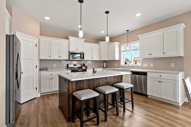 kitchen featuring a kitchen island, light wood-type flooring, light countertops, white cabinets, and appliances with stainless steel finishes