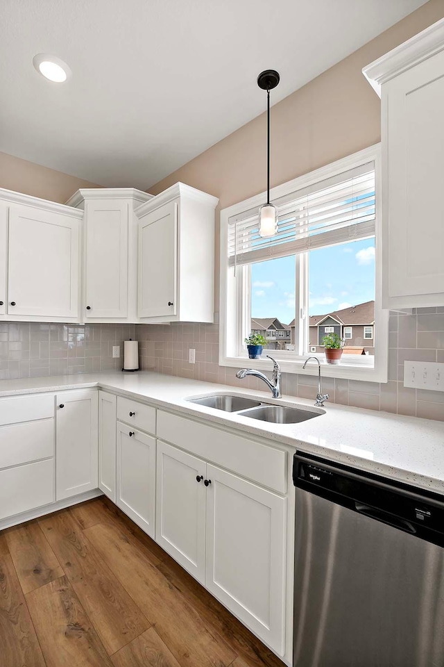 kitchen featuring hanging light fixtures, wood finished floors, dishwasher, a sink, and white cabinets