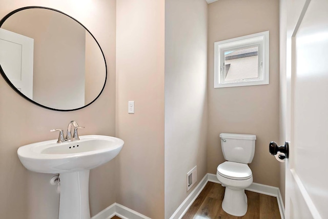 half bath with baseboards, a sink, wood finished floors, and toilet