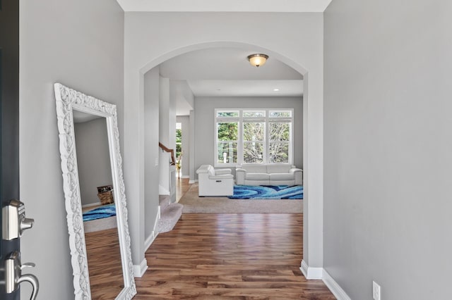 hall with arched walkways, baseboards, wood finished floors, and stairway
