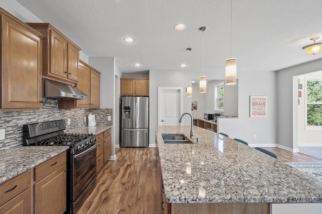 kitchen featuring a sink, decorative backsplash, under cabinet range hood, stainless steel refrigerator with ice dispenser, and gas range oven