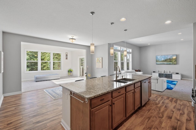kitchen with wood finished floors, open floor plan, an island with sink, a sink, and dishwasher