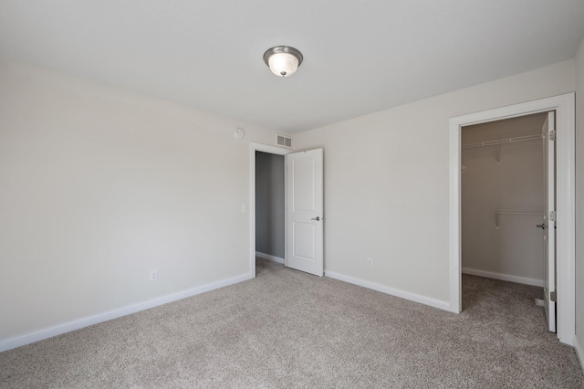 unfurnished bedroom with carpet floors, baseboards, a walk in closet, and visible vents