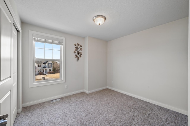 carpeted empty room with visible vents, a textured ceiling, and baseboards