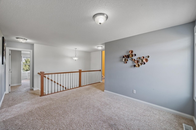 unfurnished room featuring baseboards, carpet, a textured ceiling, and visible vents