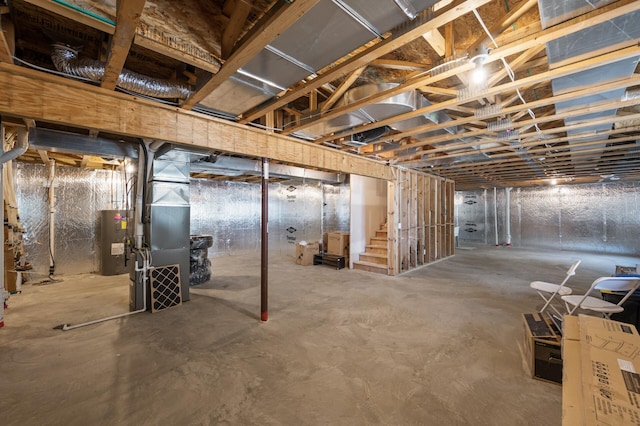 unfinished basement with heating unit, stairs, and electric water heater