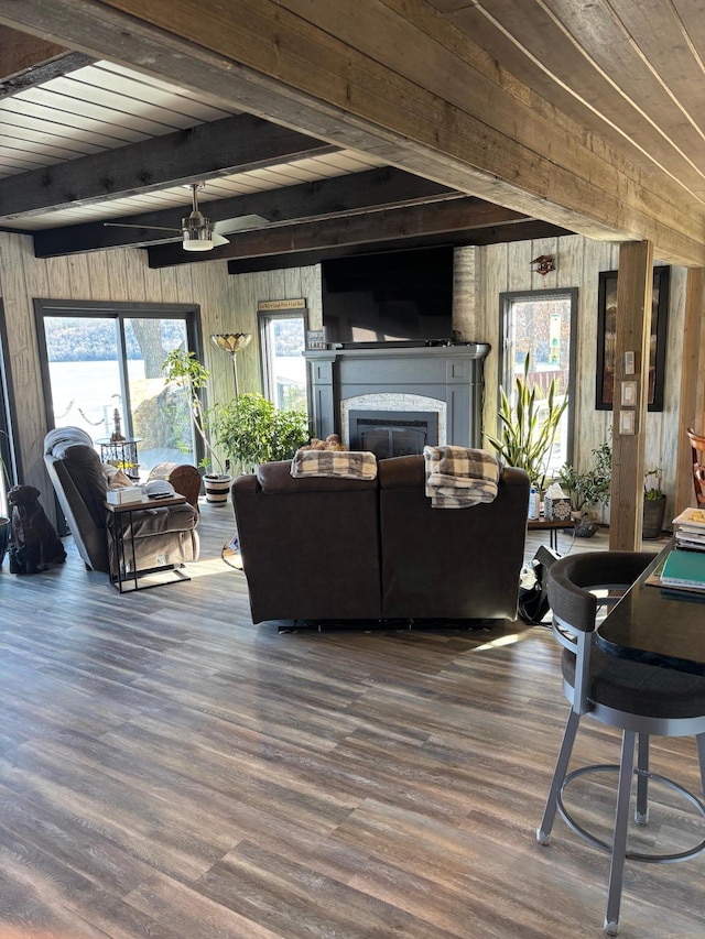 living room with wooden walls, wood finished floors, a glass covered fireplace, and beam ceiling