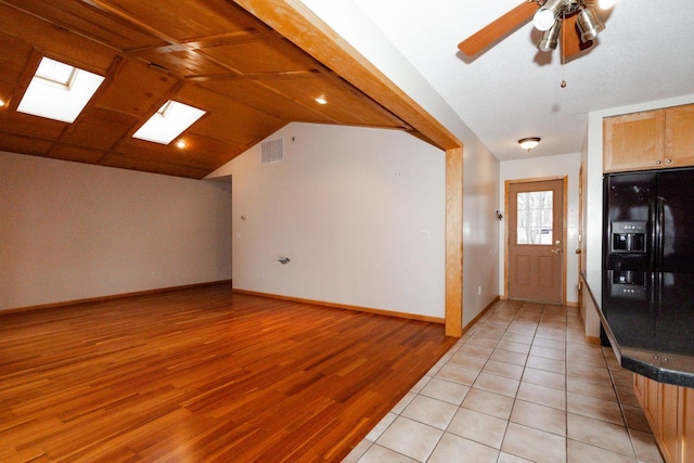 interior space featuring light wood-style flooring, lofted ceiling with skylight, baseboards, visible vents, and ceiling fan