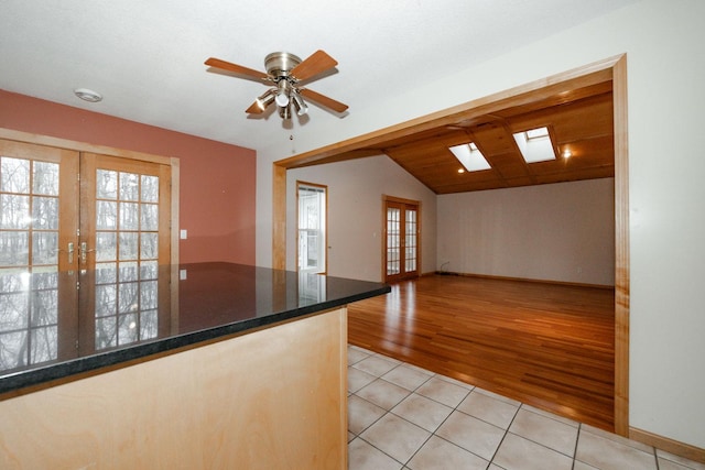kitchen featuring lofted ceiling with skylight, open floor plan, light tile patterned flooring, ceiling fan, and french doors