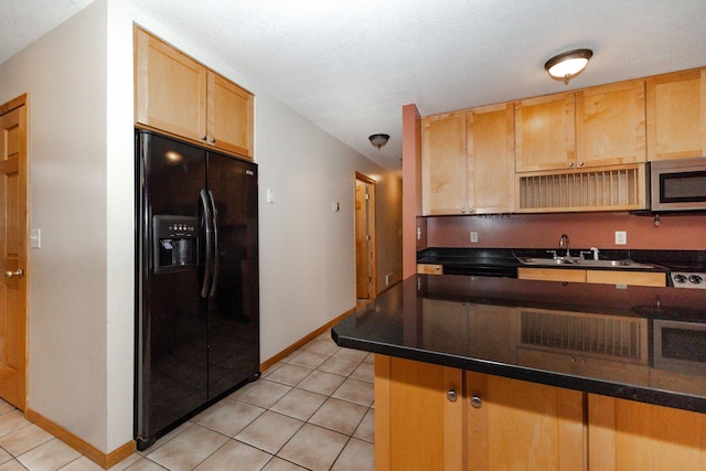 kitchen with a sink, black refrigerator with ice dispenser, stainless steel microwave, light tile patterned flooring, and baseboards
