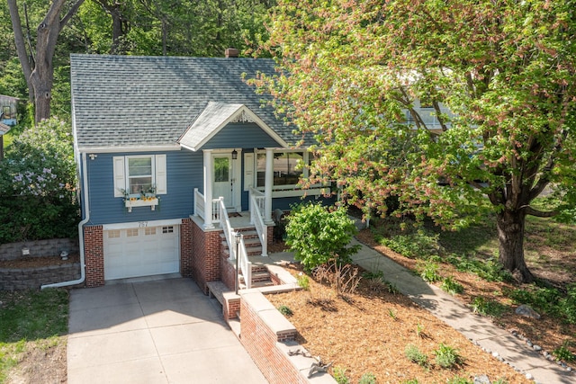 view of front of home featuring roof with shingles, driveway, a garage, covered porch, and brick siding