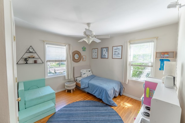 bedroom with multiple windows, wood finished floors, ceiling fan, and baseboards