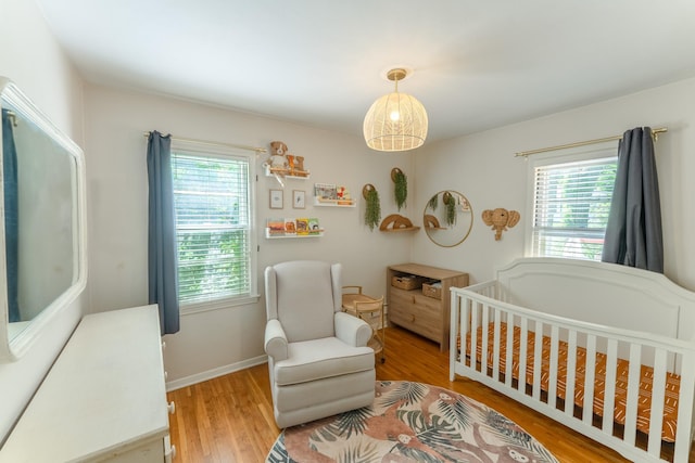 bedroom featuring light wood finished floors, multiple windows, a crib, and baseboards