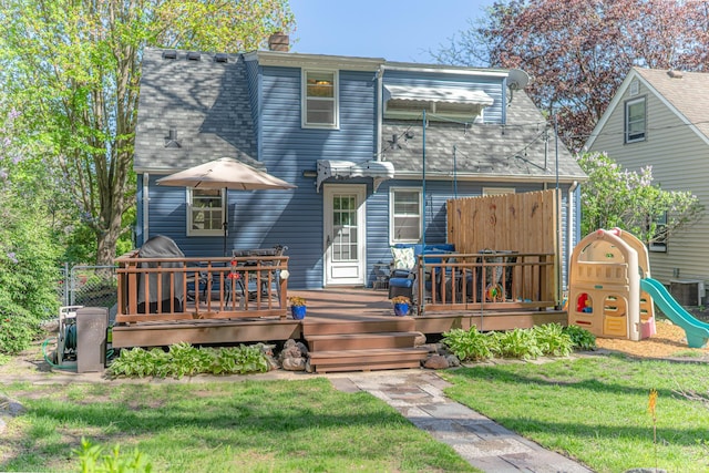 back of property featuring roof with shingles, a deck, a chimney, a playground, and cooling unit