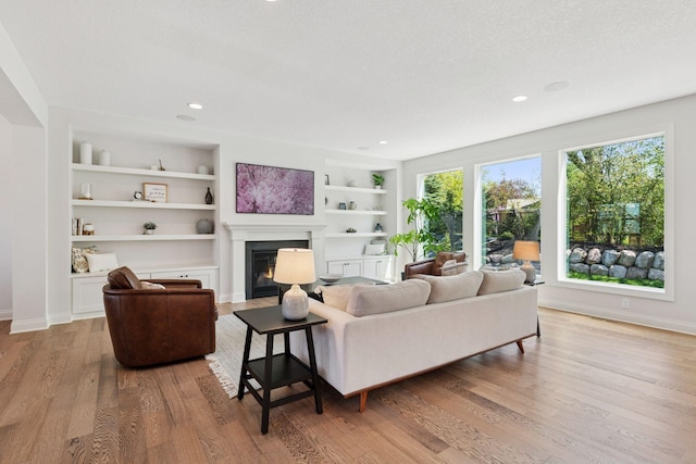 living area featuring built in features, wood finished floors, baseboards, and a glass covered fireplace