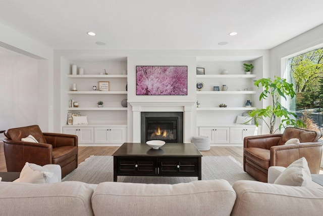living area with light wood-style floors, a glass covered fireplace, and built in features