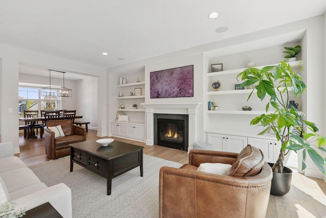 living room featuring recessed lighting, built in features, light wood-style flooring, baseboards, and a glass covered fireplace