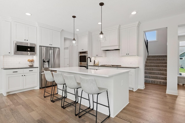kitchen with a kitchen bar, a sink, stainless steel appliances, a center island with sink, and tasteful backsplash