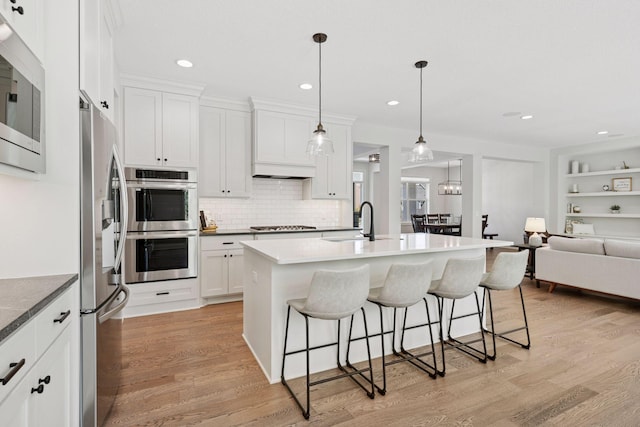 kitchen with a sink, stainless steel appliances, a breakfast bar area, open floor plan, and white cabinets