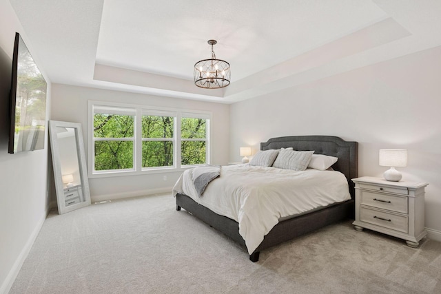 bedroom featuring a tray ceiling, light carpet, a notable chandelier, and baseboards