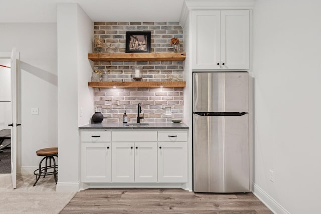 bar with freestanding refrigerator, baseboards, light wood-type flooring, and a sink