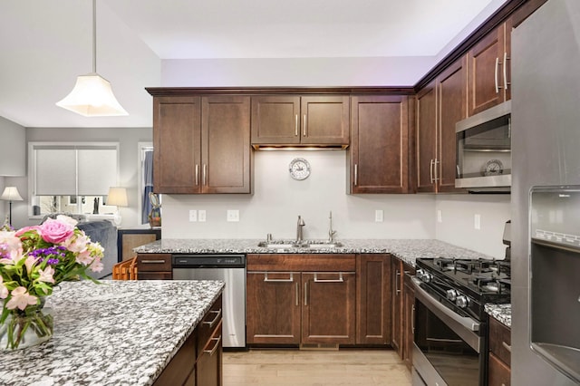 kitchen featuring light stone counters, stainless steel appliances, dark brown cabinets, a sink, and light wood-type flooring