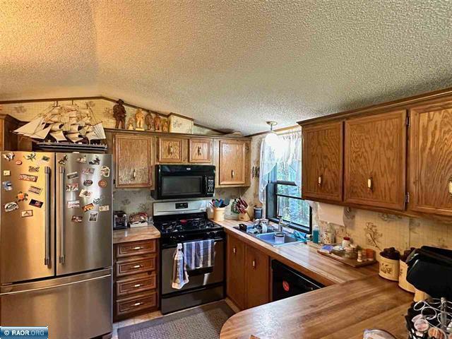 kitchen with a sink, a textured ceiling, brown cabinetry, black appliances, and light countertops