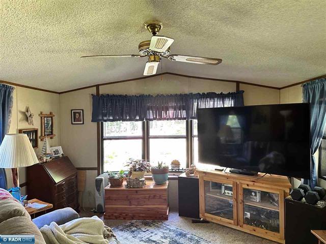 carpeted living room featuring vaulted ceiling, a textured ceiling, ceiling fan, and crown molding