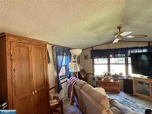 living area featuring vaulted ceiling, a ceiling fan, a textured ceiling, and carpet floors