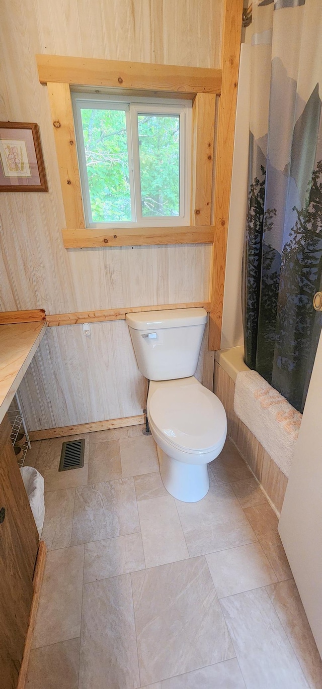 30280 County Highway 26, Holmesville Twp, MN 56501 - bathroom featuring wooden walls, shower / bathtub combination with curtain, stone finish flooring, toilet, and visible vents