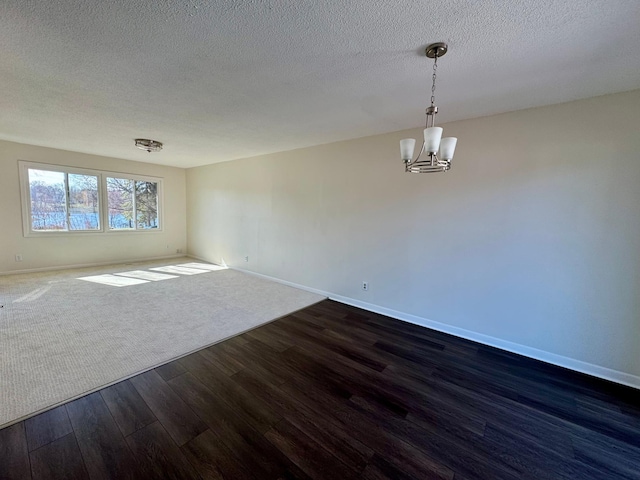 spare room with dark wood finished floors, a textured ceiling, baseboards, and an inviting chandelier