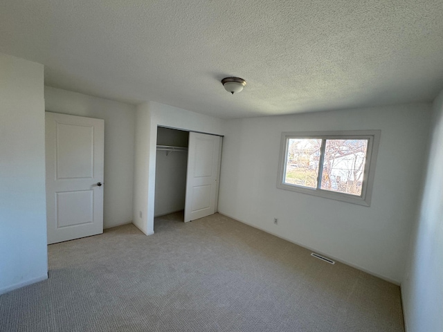 unfurnished bedroom featuring light carpet, visible vents, a textured ceiling, and a closet