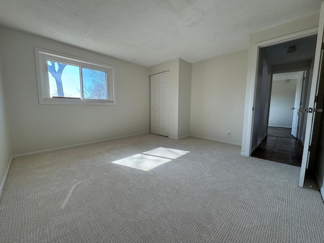 unfurnished bedroom with baseboards, carpet, a textured ceiling, and a closet