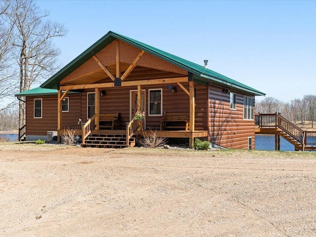 view of front facade with a porch, faux log siding, stairs, and metal roof