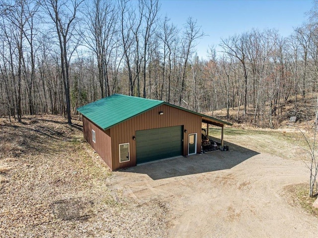 exterior space with a garage, driveway, metal roof, a view of trees, and an outbuilding