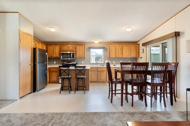 kitchen featuring a kitchen breakfast bar, a sink, appliances with stainless steel finishes, light countertops, and a kitchen island