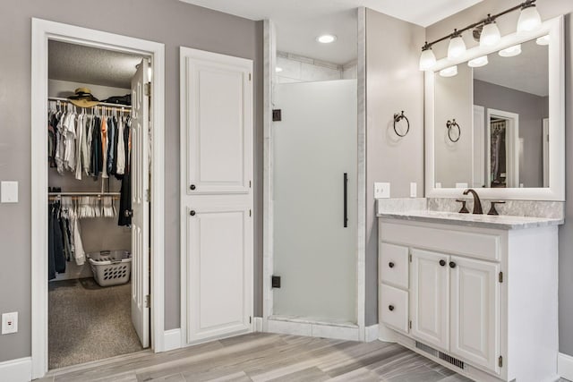 5320 132nd St W, Apple Valley, MN 55124 - bathroom featuring wood finished floors, vanity, a walk in closet, visible vents, and a stall shower