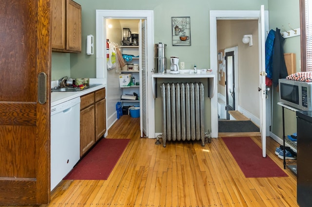 kitchen featuring radiator heating unit, white dishwasher, a sink, brown cabinetry, and stainless steel microwave