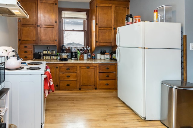 kitchen with brown cabinetry, light wood-style flooring, under cabinet range hood, and white appliances