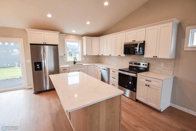 kitchen featuring light wood-style flooring, a sink, decorative backsplash, a kitchen island, and appliances with stainless steel finishes