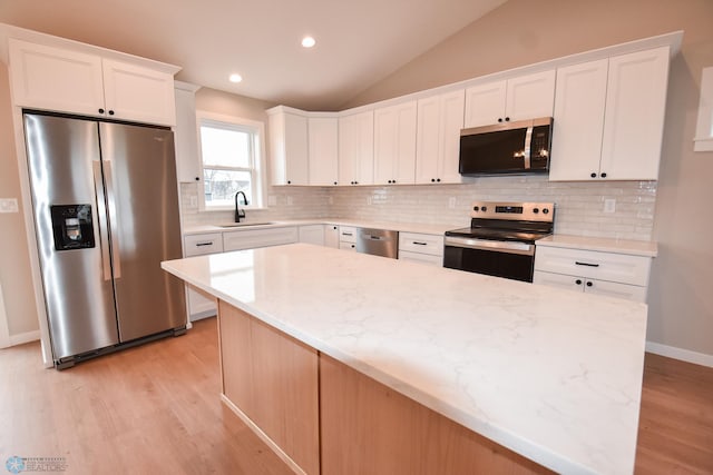kitchen featuring stainless steel appliances, a sink, light wood-style flooring, vaulted ceiling, and white cabinets