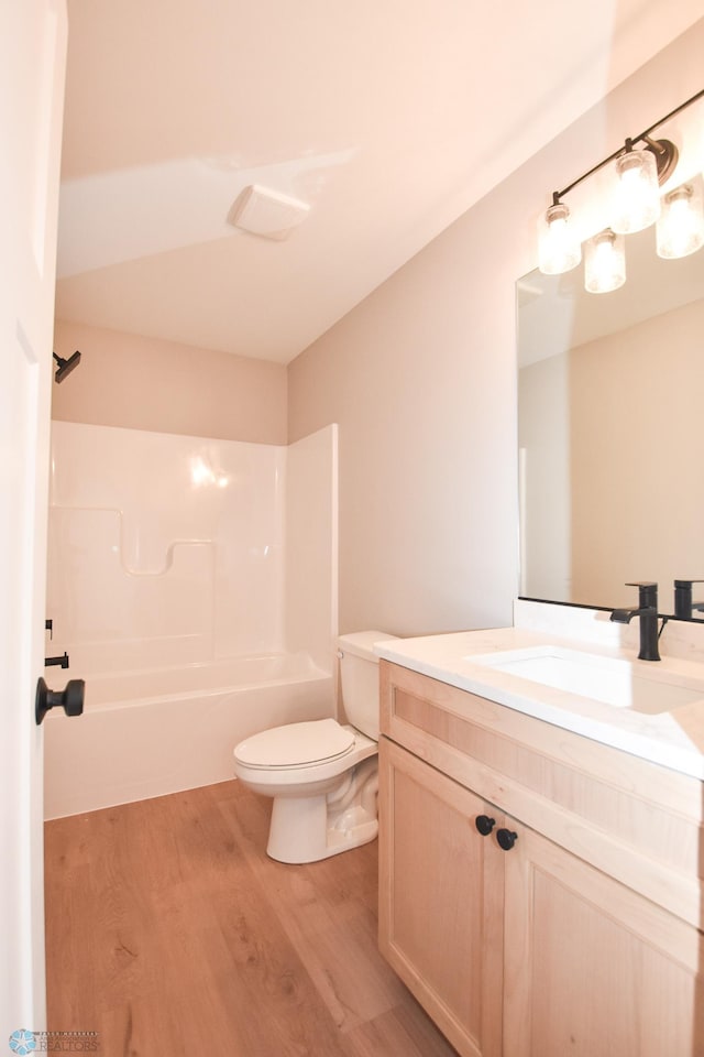 bathroom with wood finished floors, toilet,  shower combination, and vanity
