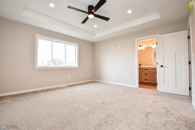 unfurnished bedroom featuring a tray ceiling, light carpet, recessed lighting, baseboards, and connected bathroom