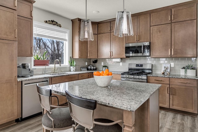 kitchen with a sink, decorative backsplash, light wood-type flooring, appliances with stainless steel finishes, and a kitchen island